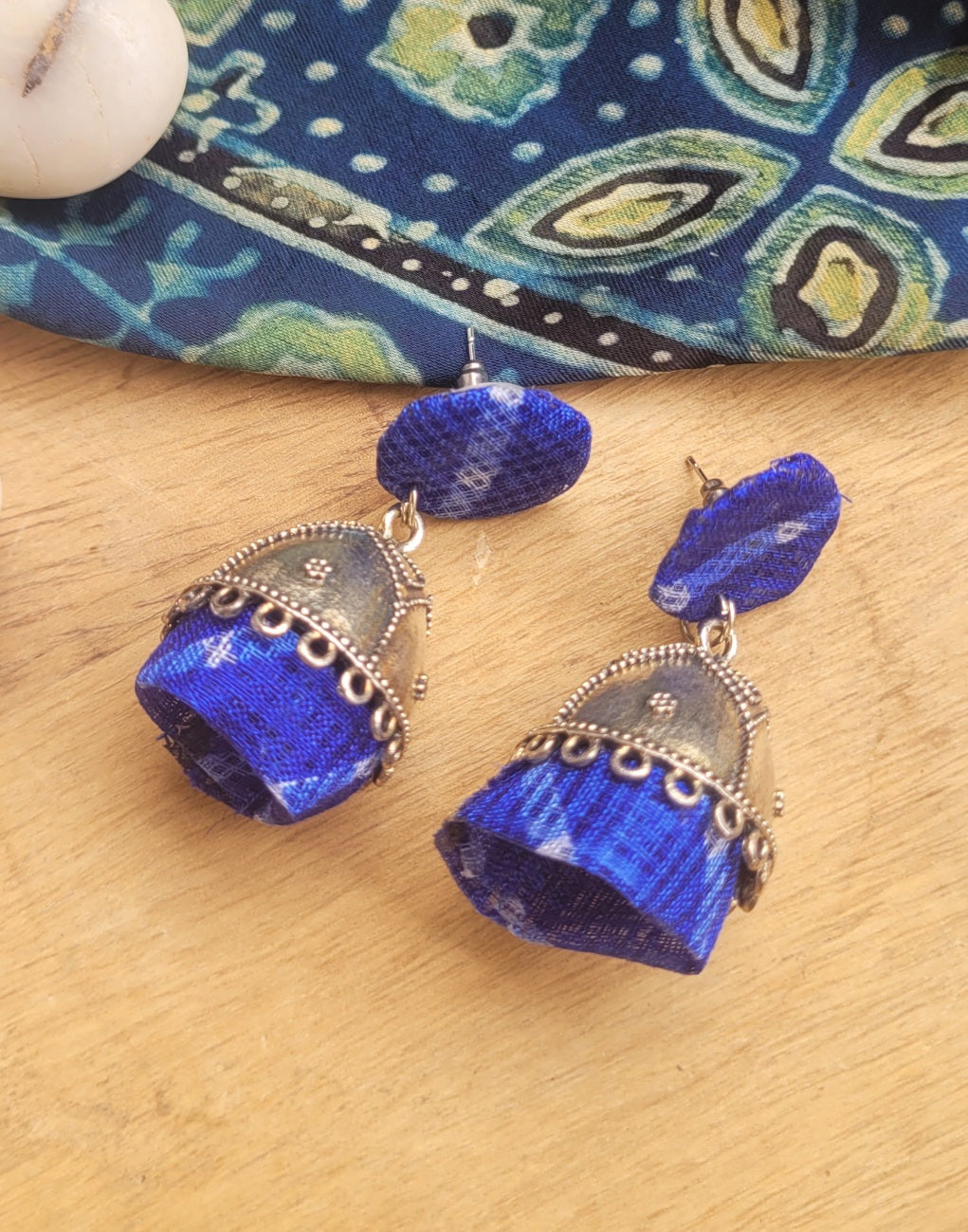 A pair of blue and silver jhumka earrings with patterned fabric bell-shaped drops.