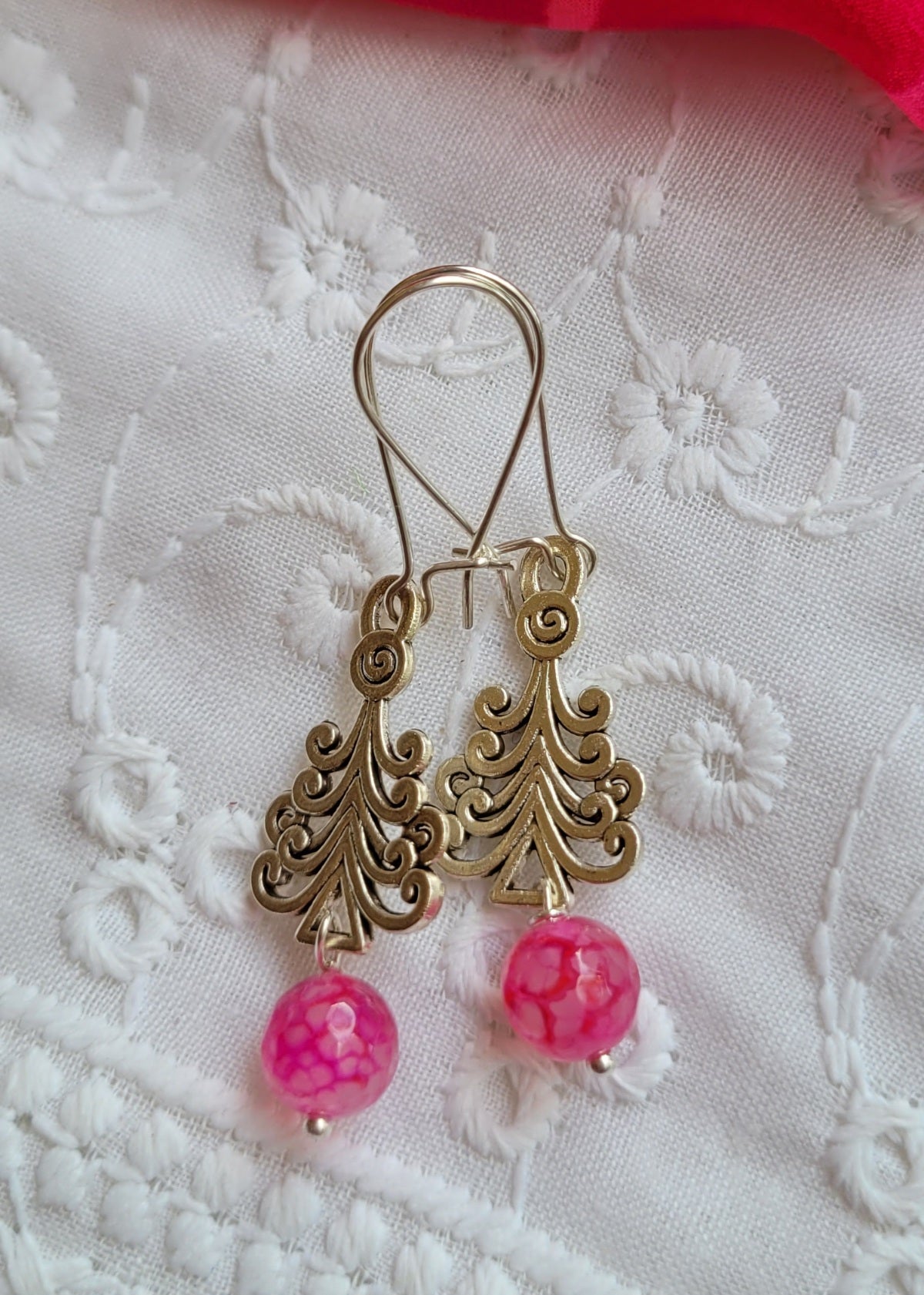 Gold earrings with pink beads on a white lace background