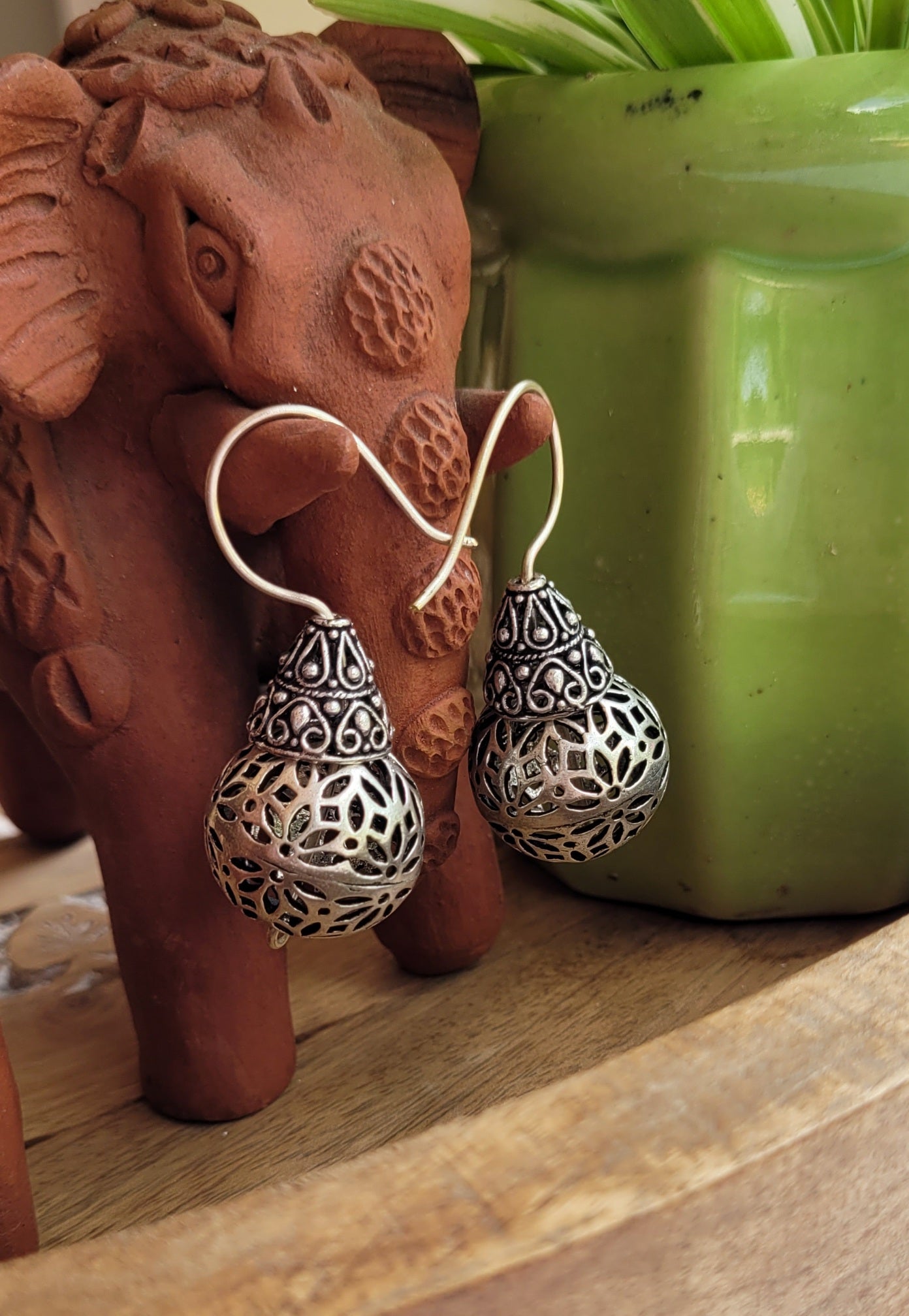 Silver earrings on a string with a terracotta elephant and green pot in the background