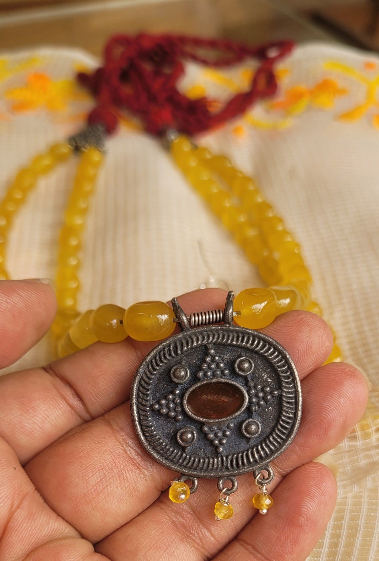 Hand holding a yellow beaded bracelet with a silver pendant on a textured fabric background