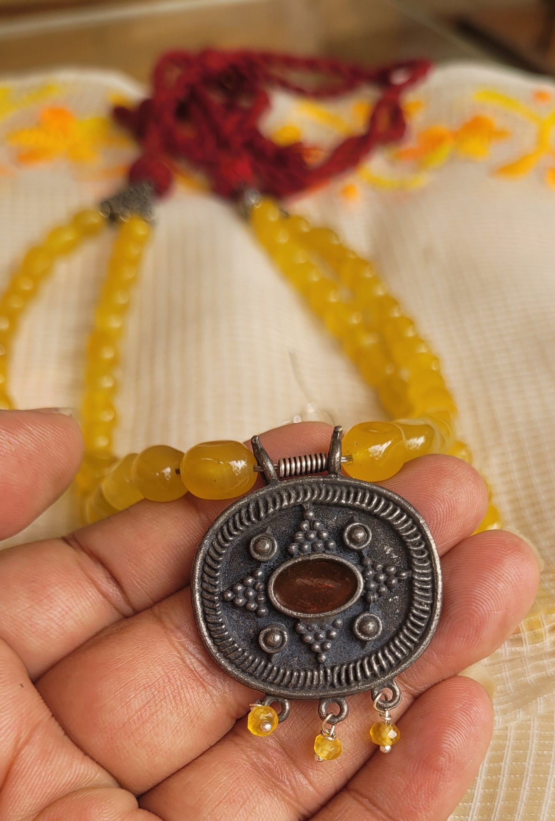Hand holding a yellow beaded bracelet with a silver pendant on a textured fabric background