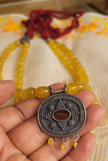 Hand holding a yellow beaded bracelet with a silver pendant on a textured fabric background
