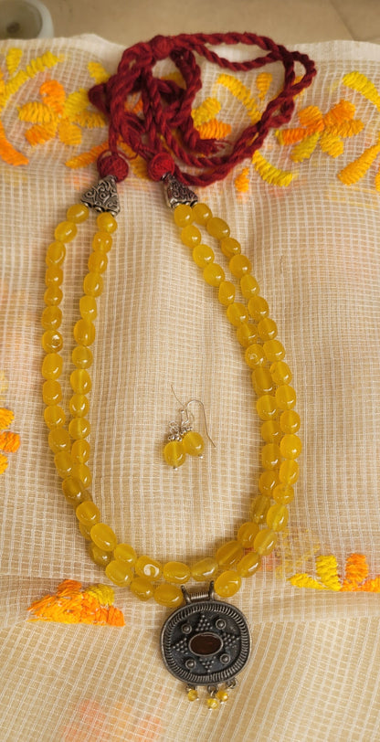 Yellow beaded necklace with a pendant on a textured fabric background