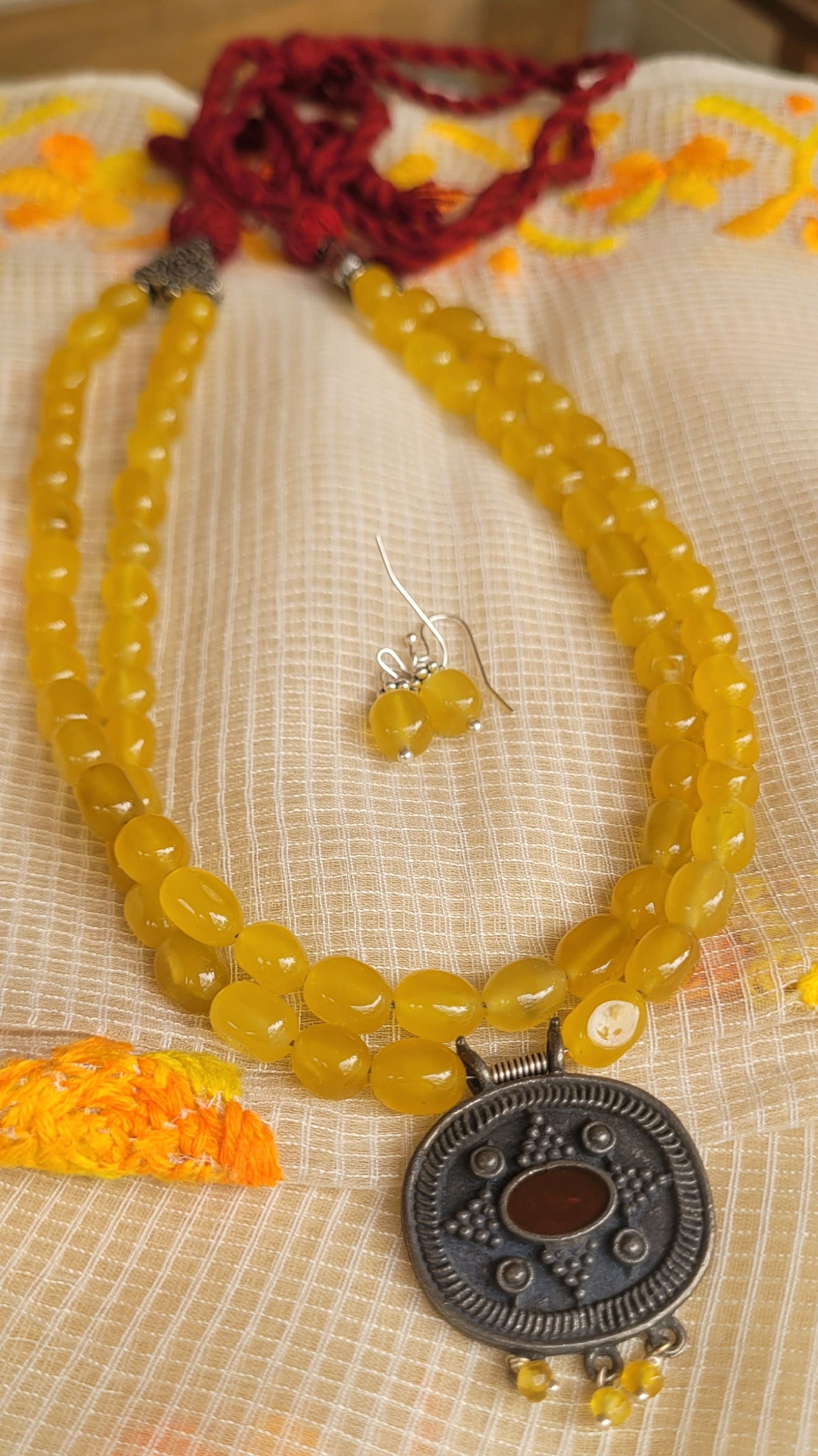 Yellow beaded necklace with a large pendant on a textured surface