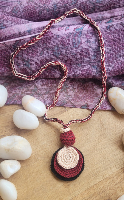 A handmade bohemian-style crochet pendant necklace with a braided chain.
