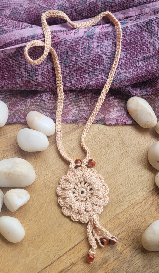 A handmade crochet necklace with a floral pendant and a long braided cord.