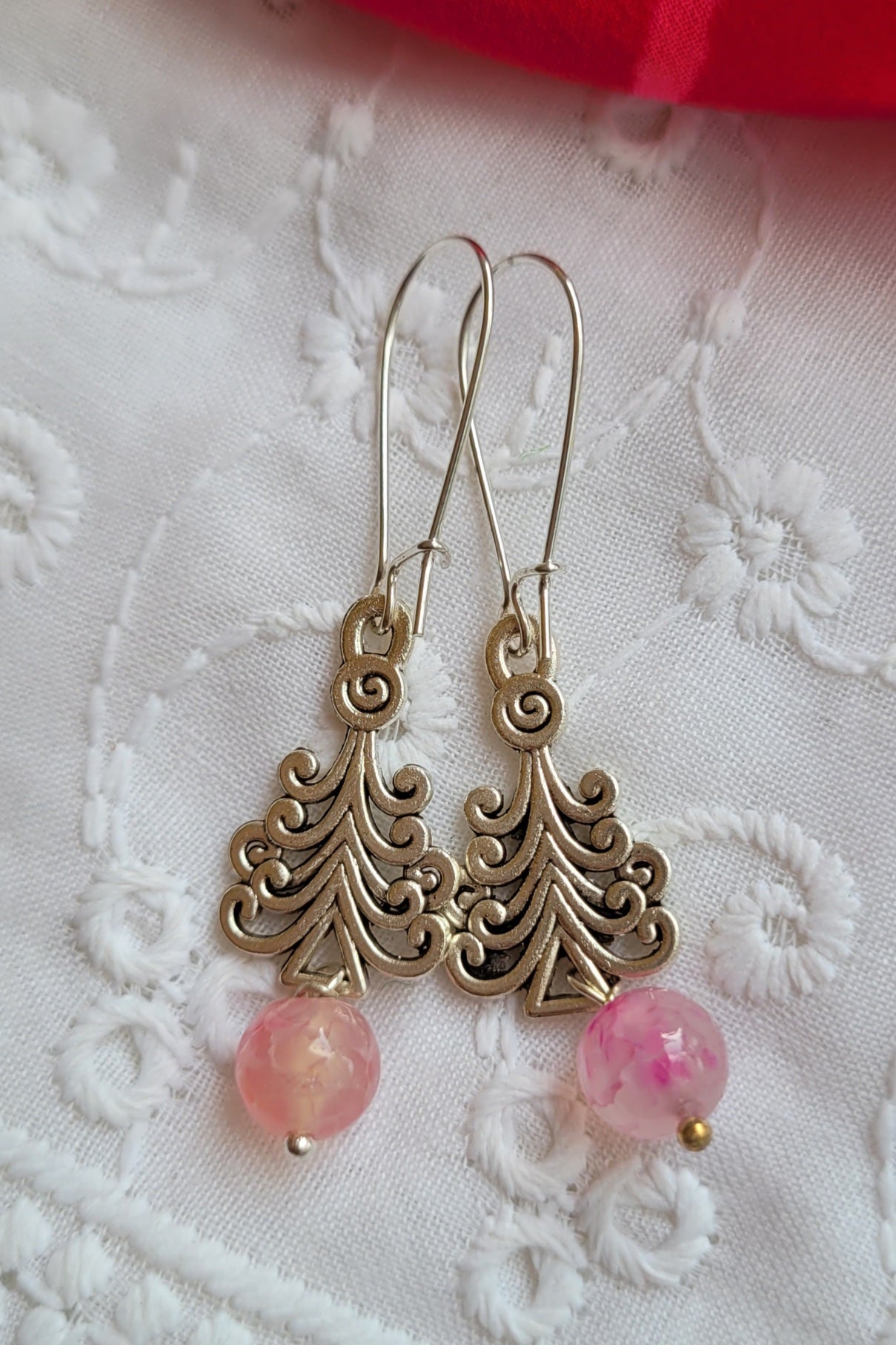 Ornate silver earrings with pink beads on a white lace background