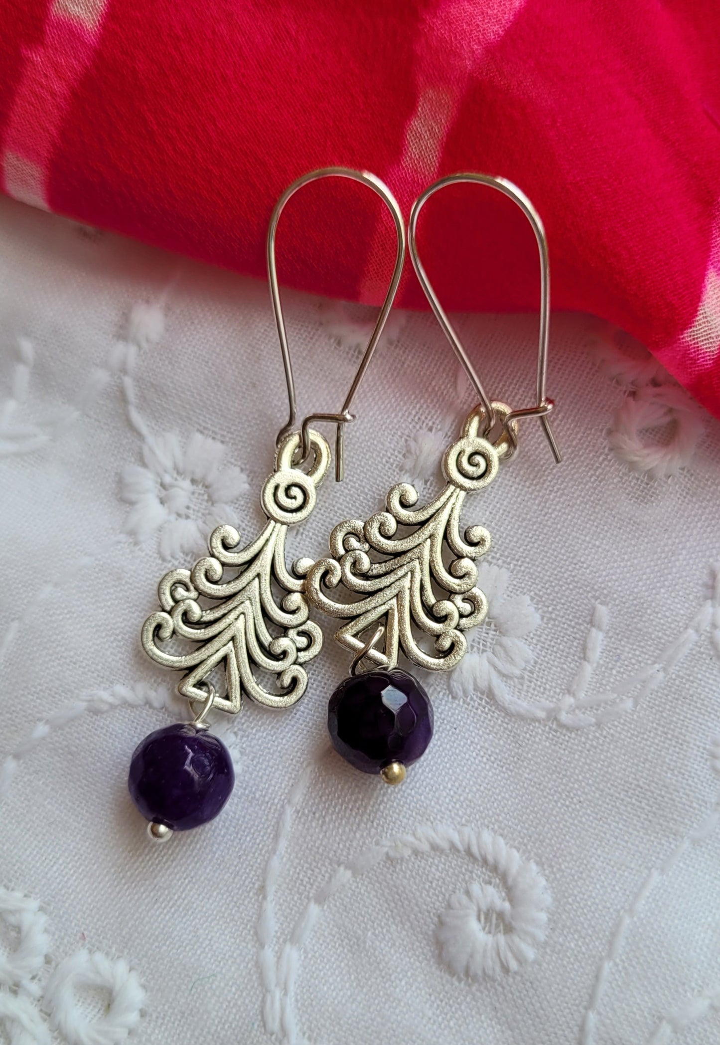 Gold earrings with purple beads on a white fabric background