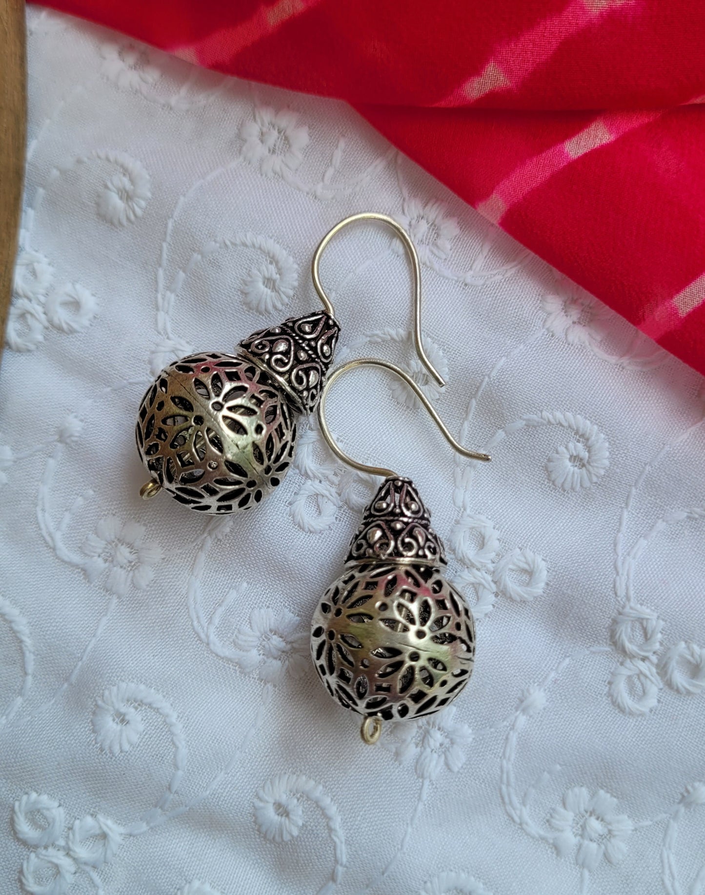 Decorative earrings on a white textured surface with a red fabric background