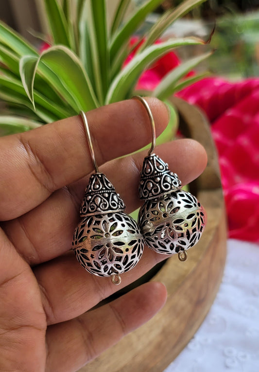 Silver earrings held in a hand with a blurred background