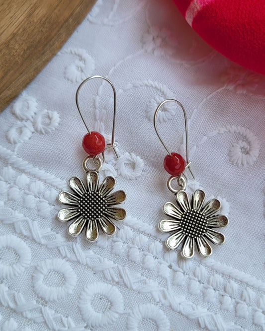 Silver flower-shaped earrings with red beads on a white lace background