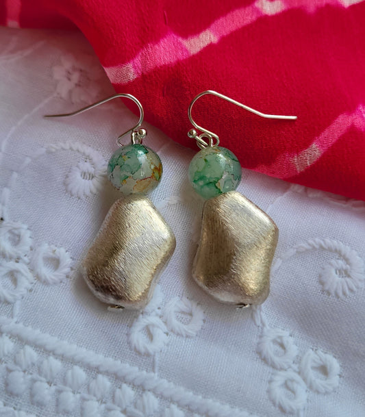 Gold earrings with green beads on a white lace fabric background