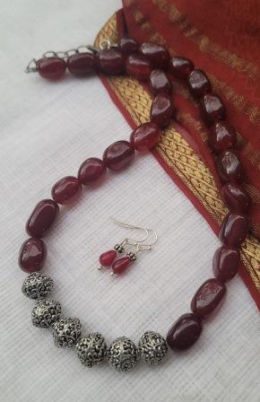 Beaded necklace and earrings with red and silver beads on a textured fabric background